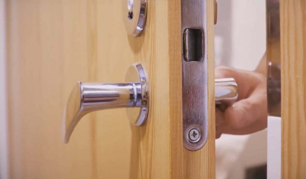 A hand turns a silver door handle against a wooden door with a keyhole