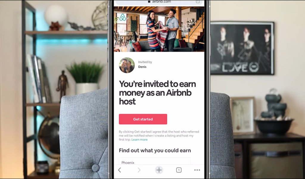 Mobile screen displaying an Airbnb host invitation, placed in a cozy room with decor