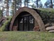 An earth-sheltered home with a grassy roof nestled in a forest.